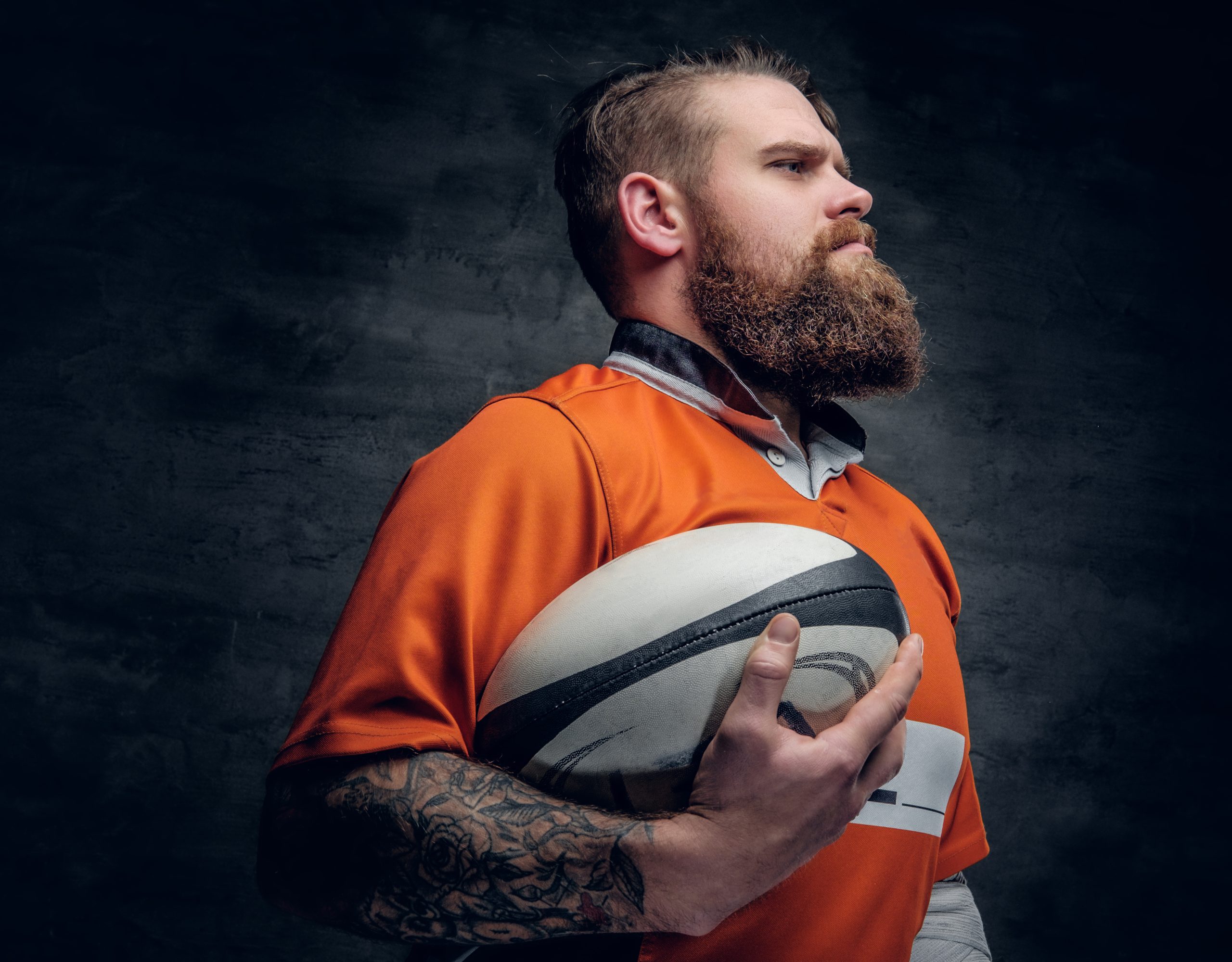 bearded rugby player holds game ball.