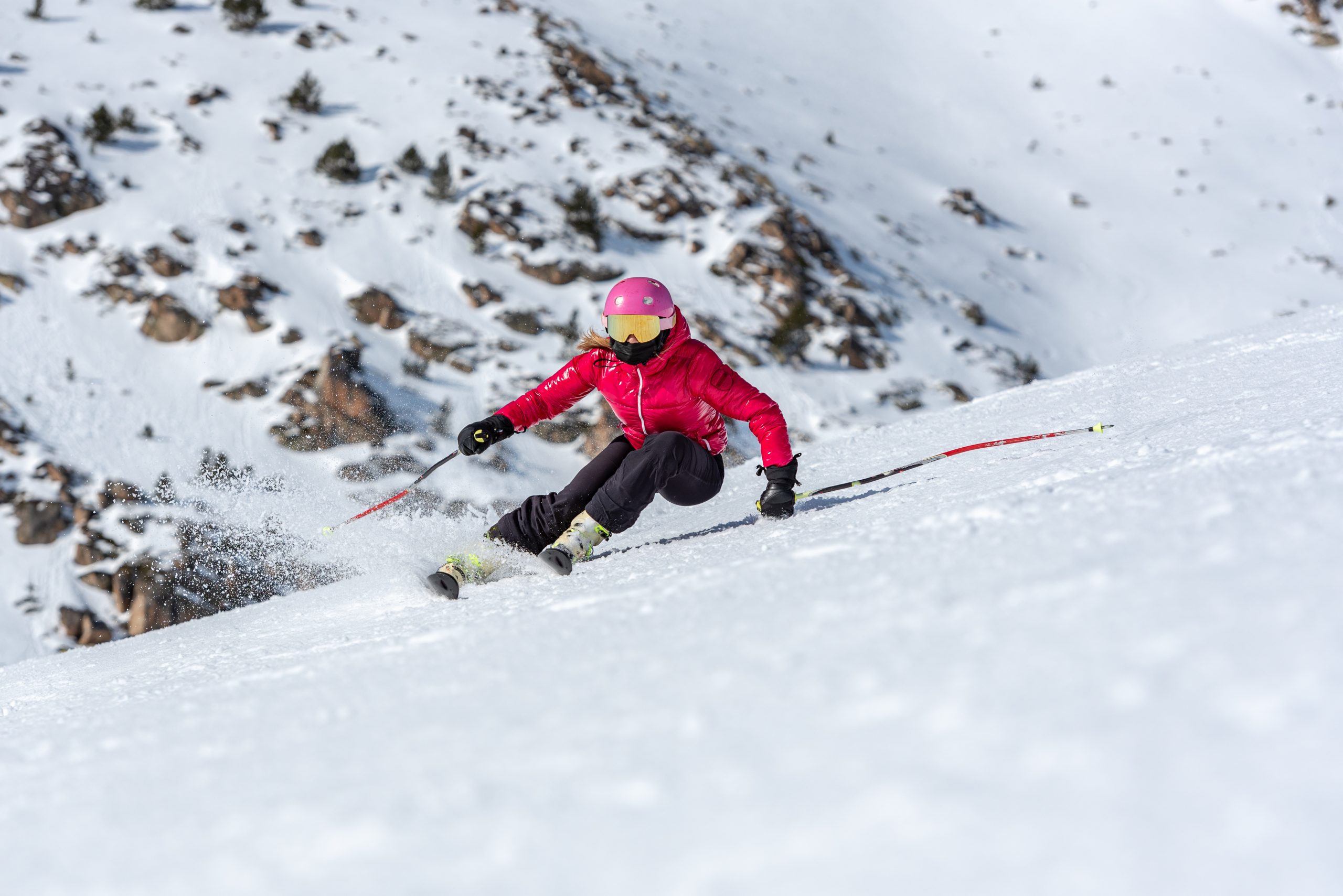 young blonde woman in ski goggles and helmet skiing on a snowy mountain slope
